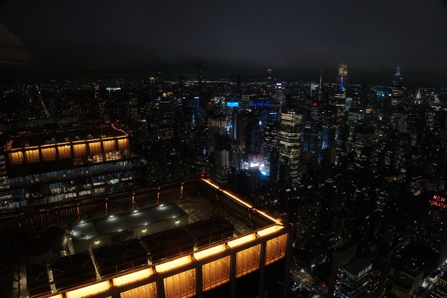 Midtown from above at night, an amber lit rooftop in the foreground.