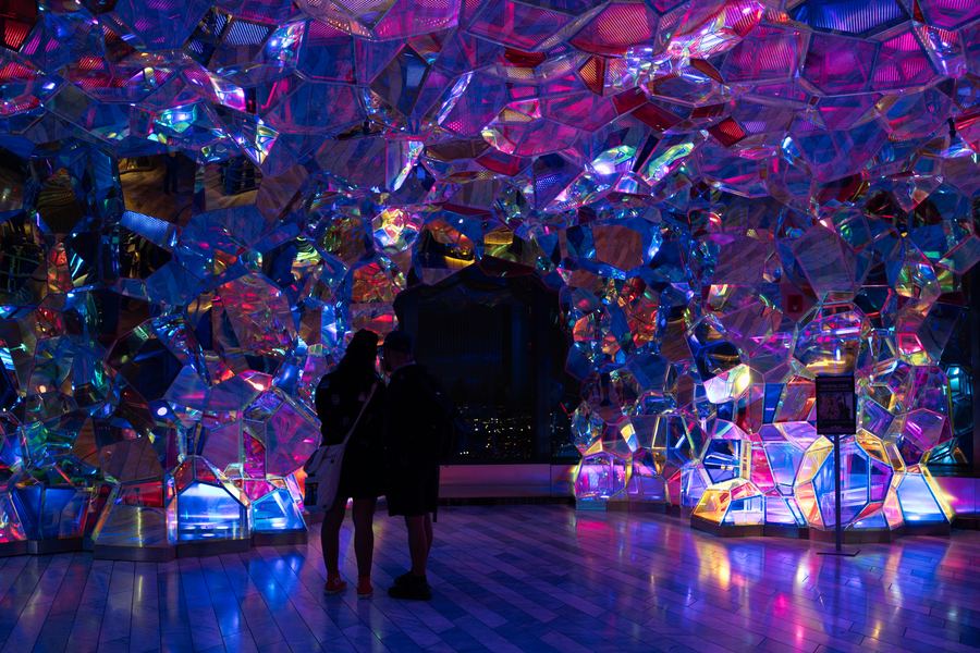 Two figures under a canopy of iridescent pink and blue crystal panels.