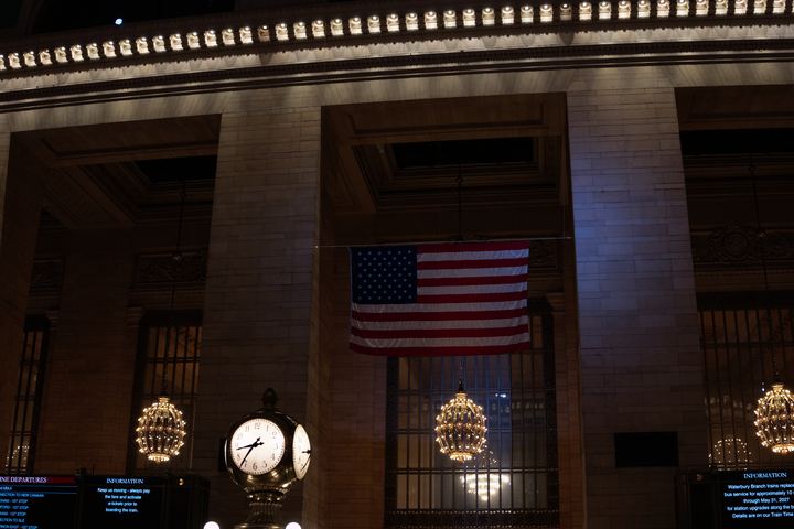 The main concourse of Grand Central Terminal, flag and clock under warm light.