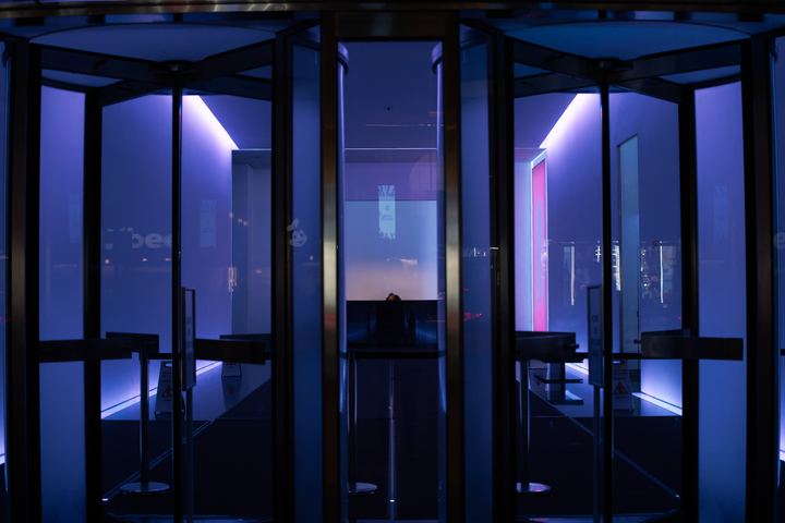 A revolving door lit from within by violet and blue tubes.
